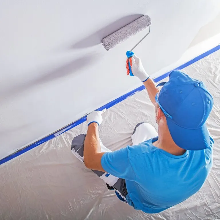 Painter rolling paint onto a ceiling with the floor covered in plastic
